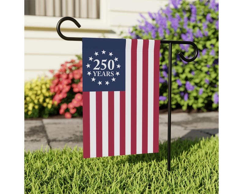 May include: A rectangular garden flag featuring a blue canton with a circle of thirteen white stars surrounding the white text 250 YEARS, and vertical red and white stripes. The flag hangs from a black metal garden stake stand.