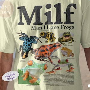 May include: Ivory t-shirt with the text "Milf Man I Love Frogs" in black. The shirt features illustrations of various colorful frogs, including a blue and black dotted frog and a bright orange frog.