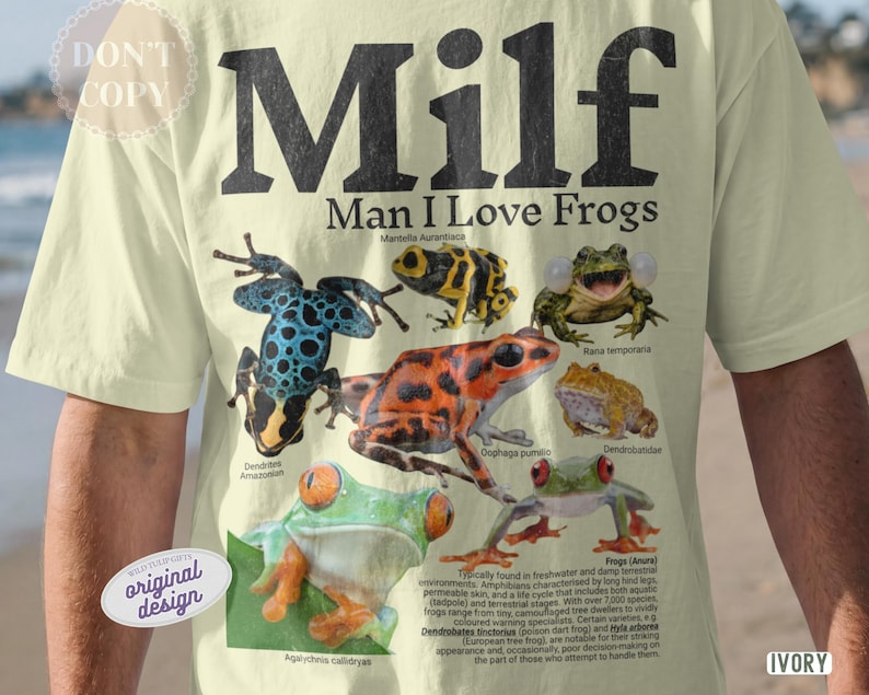 May include: Ivory t-shirt with the text "Milf Man I Love Frogs" in black. The shirt features illustrations of various colorful frogs, including a blue and black dotted frog and a bright orange frog.