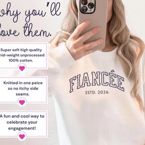 May include: White sweatshirt with the word "FIANC&Eacute;E" in navy blue block letters and "ESTD. 2026" underneath. The sweatshirt is made of 100% cotton and is a fun way to celebrate an engagement.