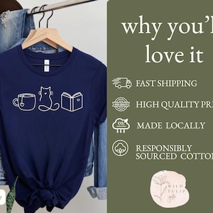May include: Navy blue t-shirt with a white graphic of a teacup, cat, and book. The text "why you'll love it" is on the right side of the shirt. The shirt is made of responsibly sourced cotton.