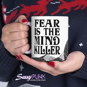 May include: White ceramic mug with black text that reads "Fear is the mind killer" in a retro font. The mug has a black and white graphic of mountains on the bottom.