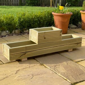 May include: A wooden planter box with two levels. The top level is a smaller rectangular box, and the bottom level is a longer rectangular box. The planter is made of natural wood and has a rustic look.