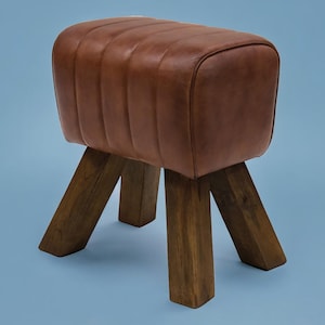Puede incluir: Un taburete de cuero marr&oacute;n y madera con la parte superior redondeada y cuatro patas. El taburete est&aacute; hecho de madera marr&oacute;n oscura y tiene un asiento de cuero marr&oacute;n.