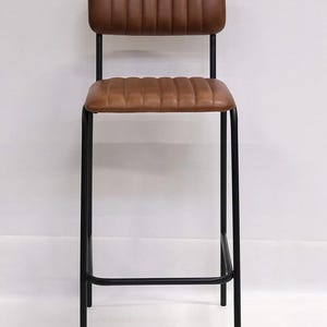 May include: A brown leather bar stool with a black metal frame. The seat and backrest are padded with a ribbed design. The stool has a footrest and is suitable for a kitchen or bar setting.