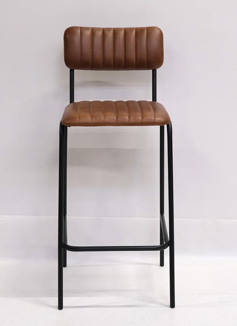 May include: A brown leather bar stool with a black metal frame. The seat and backrest are padded with a ribbed design. The stool has a footrest and is suitable for a kitchen or bar setting.