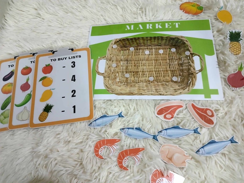 Puede incluir: Un conjunto colorido de tarjetas educativas con im&aacute;genes de frutas, verduras y otros alimentos. Las tarjetas tienen n&uacute;meros y las palabras "To Buy Lists" impresas en ellas. Tambi&eacute;n hay un cartel de mercado verde y blanco con una cesta de mimbre.