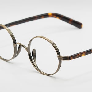 Puede incluir: Gafas redondas de tono dorado con patillas de carey.