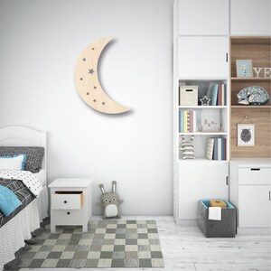 May include: A wooden crescent moon wall decor with cut-out stars. The moon is light brown and the stars are gray. The decor is hanging on a white wall in a child's bedroom.