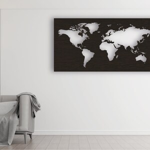 May include: A white world map cutout on a black wood background. The map is mounted on a white wall in a living room setting.