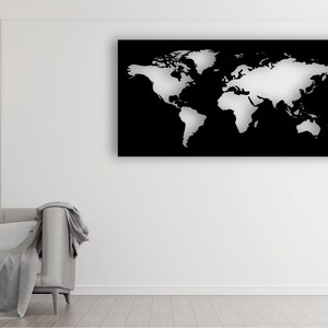 May include: A white world map cutout on a black background. The map is mounted on a white wall in a living room setting with a gray couch and a lamp.