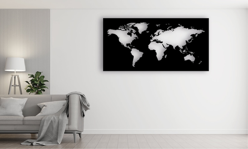 May include: A white world map cutout on a black background. The map is mounted on a white wall in a living room setting with a gray couch and a lamp.
