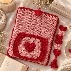 Pode incluir: Uma capa de livro retangular em crochê com listras horizontais alternadas em rosa claro e vermelho escuro, com um bolso quadrado central exibindo um motivo de coração vermelho escuro. Um pequeno fecho de botão em forma de coração fica no topo, acompanhado por um marcador de página vertical correspondente feito de corações de crochê vermelhos e rosas unidos com uma borla na ponta.