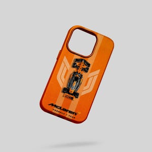May include: Orange phone case with a Formula 1 race car design. The case has a vertical stripe pattern and the McLaren Formula 1 Team logo. The phone case is designed to fit a smartphone.