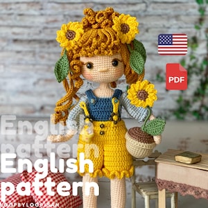 Puede incluir: Patrón de muñeca de crochet en formato PDF. La muñeca lleva un atuendo azul y amarillo y tiene un girasol en la mano. La muñeca tiene ojos marrones y cabello rubio con una corona de girasoles.