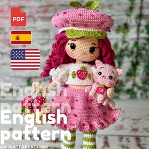 Puede incluir: Muñeca de ganchillo hecha a mano vestida con un atuendo rosa con temática de fresa, que incluye un sombrero y una falda. La muñeca tiene cabello rojo, una parte superior blanca con una aplicación de fresa y sostiene un gato rosa. Incluye el texto "English pattern".