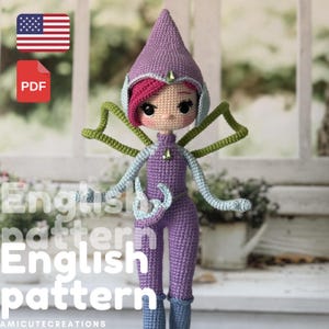 May include: A handmade crochet doll in a purple jumpsuit and pointed hat, with green and blue details. The doll has pink hair and large eyes. The image includes a PDF icon and a US flag icon.