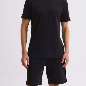 Könnte beinhalten: Ein schwarzes T-Shirt und ein passendes schwarzes Shorts-Set. Das T-Shirt hat kurze Ärmel und die Shorts sind knielang. Die Person trägt schwarze Turnschuhe mit weißen Sohlen.