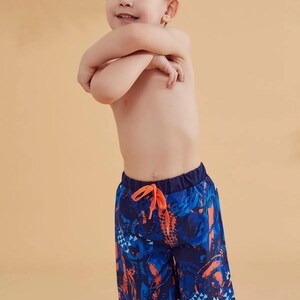 Peut inclure: Short de bain bleu et orange &agrave; motifs avec taille &eacute;lastique et cordon de serrage. Le short pr&eacute;sente un motif vibrant avec des formes g&eacute;om&eacute;triques et des motifs abstraits. Le gar&ccedil;on porte le short de bain.