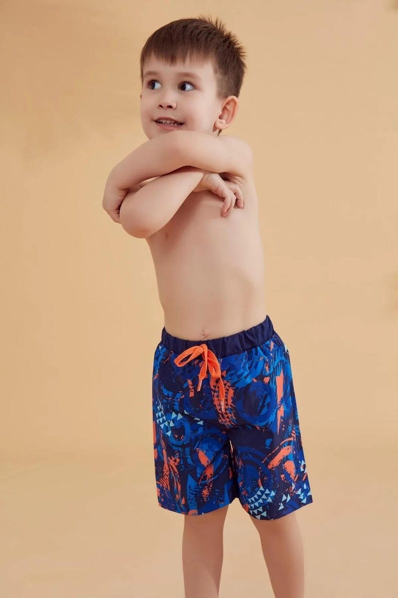 Peut inclure: Short de bain bleu et orange &agrave; motifs avec taille &eacute;lastique et cordon de serrage. Le short pr&eacute;sente un motif vibrant avec des formes g&eacute;om&eacute;triques et des motifs abstraits. Le gar&ccedil;on porte le short de bain.