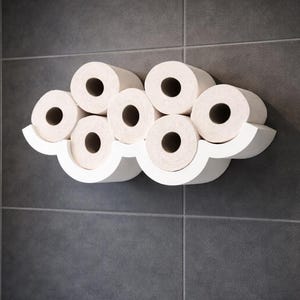 Könnte beinhalten: Ein weißer, wolkenförmiger Toilettenpapierhalter an einer dunkelgrauen gefliesten Wand. Der Halter enthält sieben Rollen Toilettenpapier. Das Design ist modern und minimalistisch, passend für ein Badezimmer.