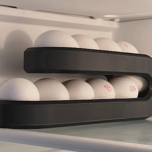 May include: A black, two-tiered egg holder inside a refrigerator. Each tier holds six white eggs. The eggs have red ink stamps. The holder is a curved, modern design.