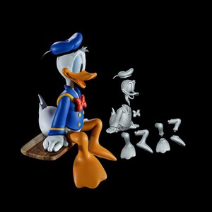 May include: A detailed figurine of Donald Duck, seated on a wooden plank, with a blue sailor suit, bow tie, and hat. The figure is accompanied by disassembled gray parts, including a head, torso, and feet, against a black background.