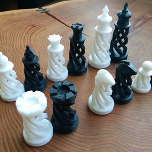 Op de afbeelding: Een schaakspel met zwarte en witte stukken, gerangschikt op een houten oppervlak. De stukken omvatten pionnen, torens, paarden, lopers, een dame en een koning. De schaakstukken hebben een uniek, gedraaid ontwerp.