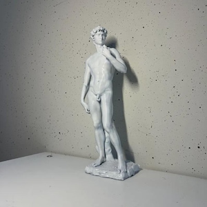 May include: A white, detailed sculpture of a nude male figure standing with one hand on his hip. The sculpture is on a white base.