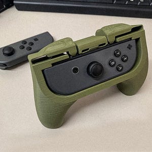 以下が含まれることがあります： テクスチャ加工されたグリップが付いた緑と黒のNintendo Switchコントローラー。コントローラーは折りたたみ式デザインで、A、B、X、Yのラベルが付いたボタンがあります。