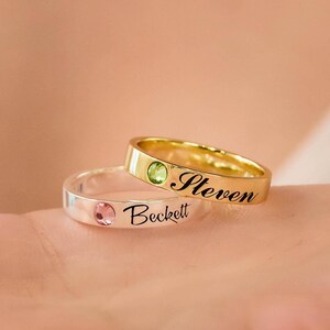 May include: Two personalised rings with a green and pink gemstone. The gold ring says "Steven" and the silver ring says "Beckett".