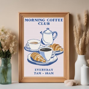 Puede incluir: Una impresión enmarcada con una ilustración azul y blanca de café, croissants y una tetera. El texto dice "Morning Coffee Club Everyday 7AM - 10AM".