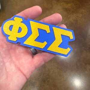 May include: A blue and gold felt letter patch with the Greek letters Phi Sigma Sigma.