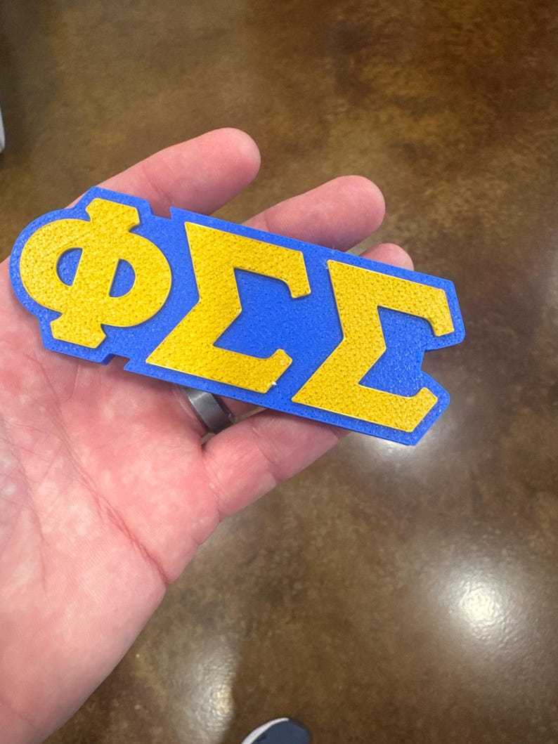 May include: A blue and gold felt letter patch with the Greek letters Phi Sigma Sigma.