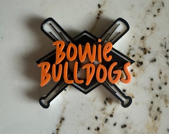 以下が含まれることがあります： オレンジ色の「Bowie Bulldogs」という文字が入った、黒と白の野球をテーマにしたロゴ。ロゴはダイヤモンド型で、2本の交差した野球のバットが描かれている。