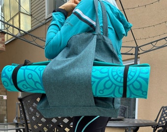 May include: A dark teal fabric tote bag with two shoulder straps, designed to carry a rolled-up bright turquoise yoga mat. The mat features a dark teal mandala-style circular pattern and is secured with black elastic straps on both ends.