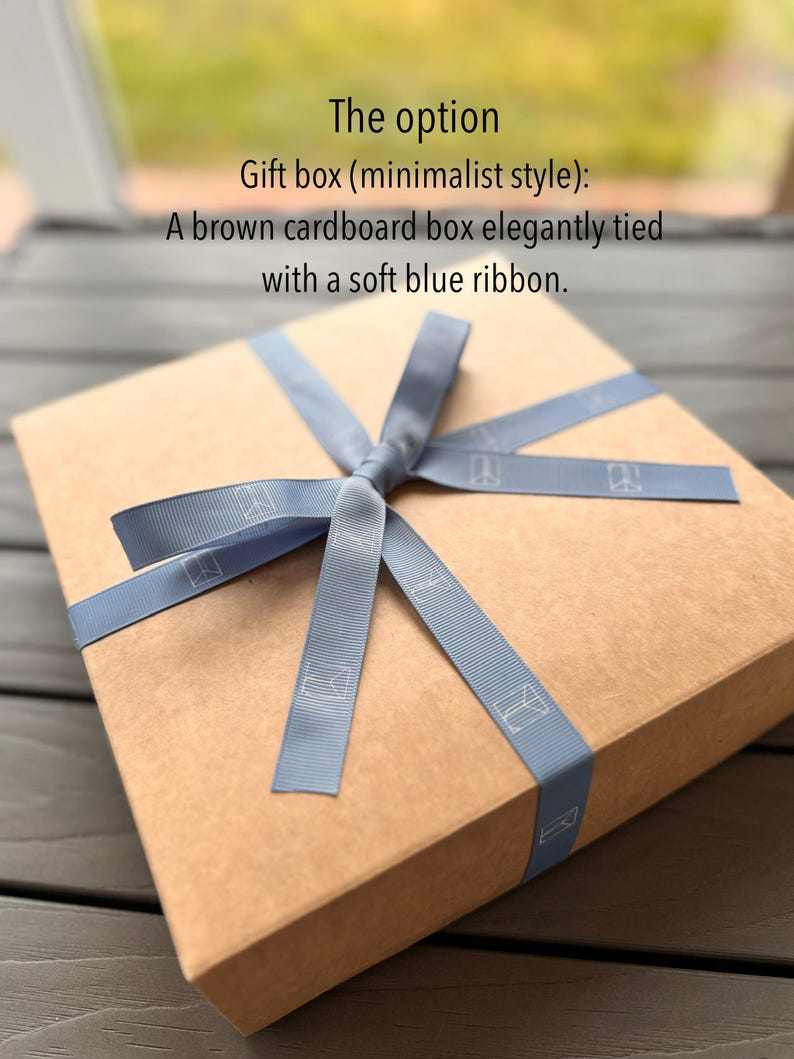 Puede incluir: Una caja de regalo de cart&oacute;n marr&oacute;n atada con una cinta azul claro. La caja es rectangular y de estilo minimalista. La cinta tiene un dise&ntilde;o sutil.