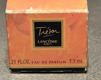 Puede incluir: Una pequeña caja naranja de perfume Lancôme Trésor. La caja tiene una etiqueta negra con el nombre "Trésor" en cursiva y "Lancôme Paris" debajo. La caja dice ".25 FL.OZ. EAU DE PARFUM 7,5 ml".