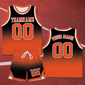 May include: A basketball uniform set in black and orange, featuring a tank top and shorts. The tank top and shorts have the text "TEAMNAME" and "00" in white. The back of the tank top has the text "YOUR NAME" and "00". The uniform has white trim.