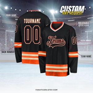 May include: Black hockey jersey with orange and white stripes. The jersey has "Teams" written on the front in orange and white lettering. The back of the jersey has a blank space for a name and number.