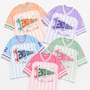 May include: Five V-neck jerseys in peach, purple, light blue, green, and pink. Each features a pennant graphic with the text 2ND GRADE and Mrs. Smith, plus the number 2 on the sleeves. The shirts have vertical stripes and ribbed trim.