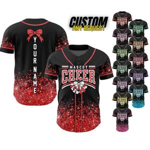 May include: Black baseball jersey with red glitter accents and a bow design. The front features "MASCOT CHEER" in red and white, with a bow graphic. The back has a bow and space for a name. Additional jerseys in various colors are displayed.