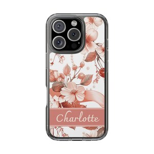 Op de afbeelding: Transparante telefoonhoes met een bloemenpatroon in perzik- en wittinten. Het ontwerp bevat bloemen, bessen en de naam "Charlotte" op een perzikbanner.