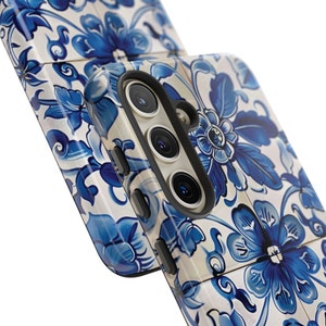 Op de afbeelding: Een witte en blauwe telefoonhoes met een bloemenpatroon. De hoes heeft een verhoogde camerabult met drie lenzen.
