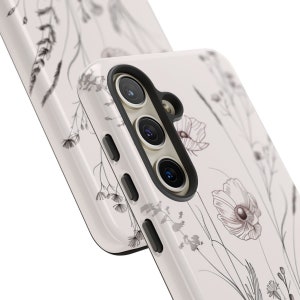 May include: A white phone case with a floral design. The case has a black camera bump with three lenses.