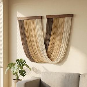 May include: A wall hanging consisting of two dark wooden horizontal bars from which long, thin, vertical cords in a gradient of brown, tan, and cream colours drape in a U-shaped curve, creating a layered, textured, and linear visual display.
