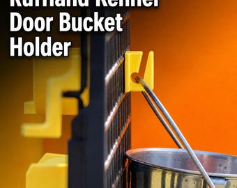 May include: A bright yellow plastic Ruffland Kennel Door Bucket Holder attached to a black wire kennel door. The holder features a hook design that supports the metal handle of a silver stainless steel bucket, keeping it securely in place.