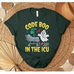May include: Dark green t-shirt featuring the text "CODE BOO IN THE ICU" in yellow and white. The design includes a ghost wearing a nurse's cap, a hospital bed, and a medical drip. A bat and stars are also included in the design.