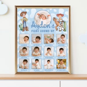 May include: A framed milestone poster with a light blue cow print background featuring cartoon cowboy characters, a central photo of a baby, and twelve smaller photos labeled one through twelve with the text Ayden's FIRST ROUND UP.