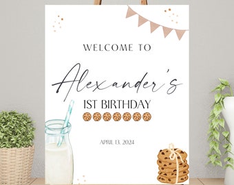 May include: Welcome to Alexander's 1st Birthday party sign with a white background, brown and white cookies, a glass of milk, and a blue and white straw. The date April 13, 2024 is printed on the sign.